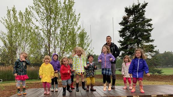 A group of young children and a teacher standing outside on a rainy day.