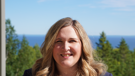 A headshot of Katie Gettman with Lake Superior and forest in the background