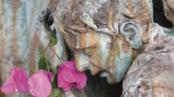 Aged statue of a person weeping with flowers