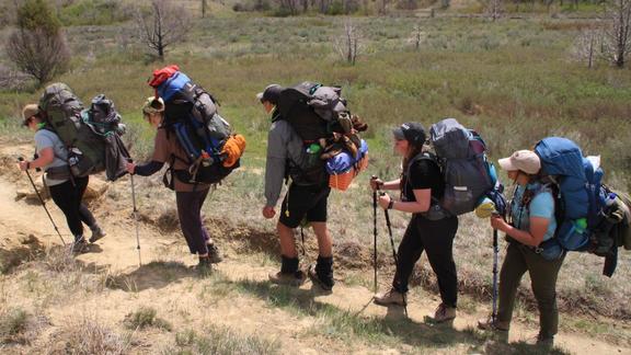 Five UMD students carrying fully-loaded backpacks and using hiking poles in the Badlands