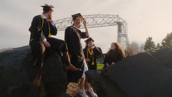 奥利维娅·纳尔逊和三位毕业生在运河公园的巨石上合影，背景是空中升降桥。