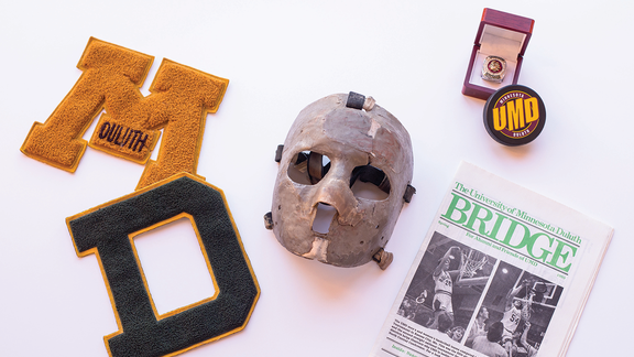 An image showing artifacts from UMD's history. Two patches, goalie mask, championship ring, hockey puck, and a Bridge magazine.