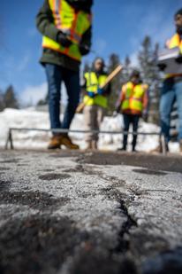 Manik Barman, Ph.D, and students conduct research of roadway cracks in Duluth, MN. Photo shows a crack in a road, with several figures in reflective vests in the background.