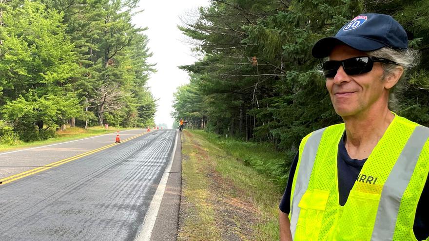 A man in a yellow vest standing by the side of the road.