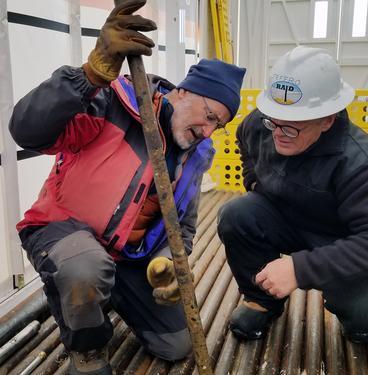Two researchers in winter clothing looking at a long sample of core ice.