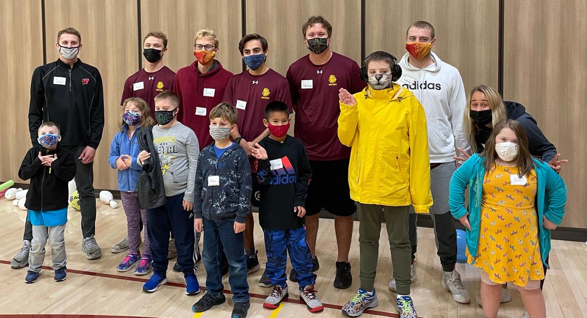 A group of children and adult sin a school gym, wearing masks.