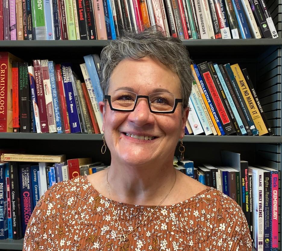 A woman with short gray hair and glasses standing in front of a bookshelf.