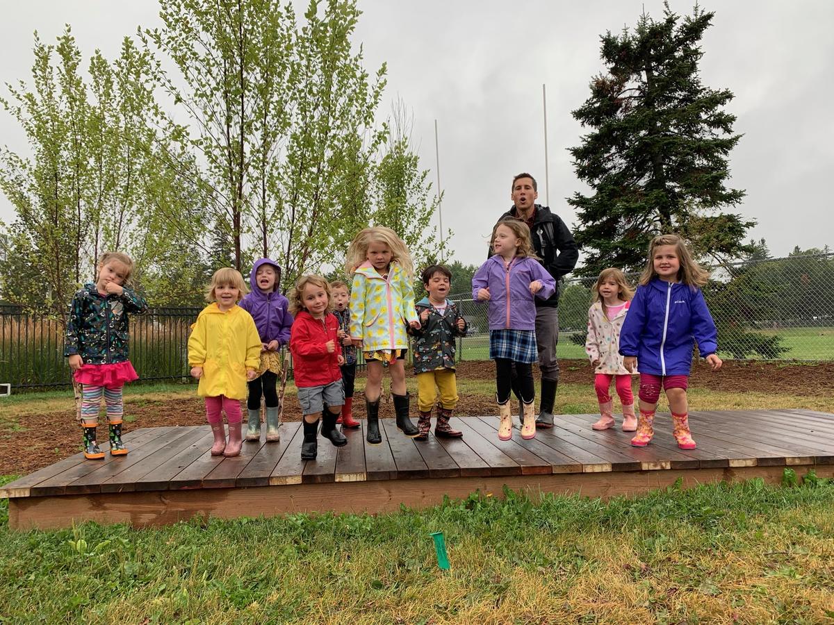 A group of young children and a teacher standing outside on a rainy day.