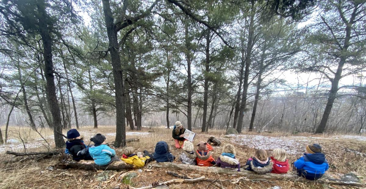 A teacher reading to a group of children sitting in the woods.