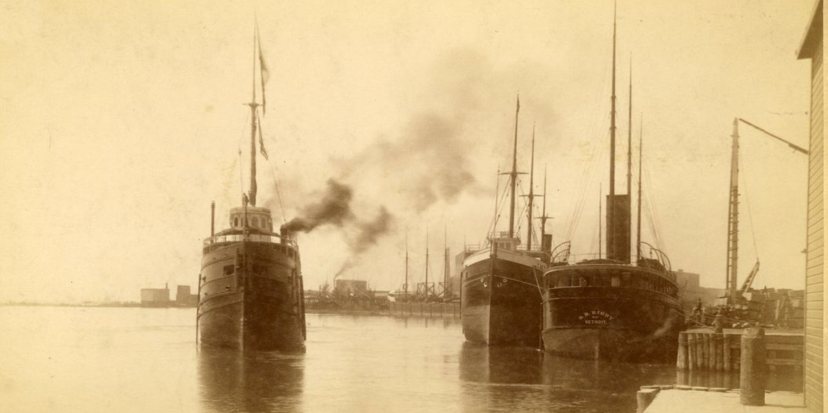 A historic sepia photograph shows boats in the Duluth harbor