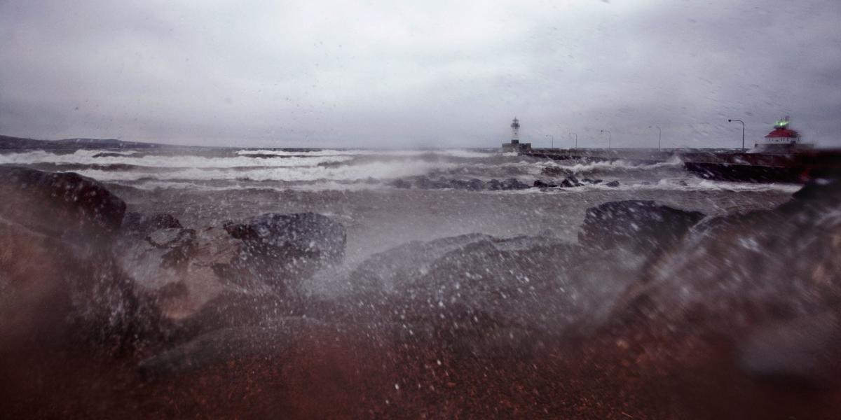 Waves roll in from Lake Superior during a storm with the Duluth entry lighthouse in the background.