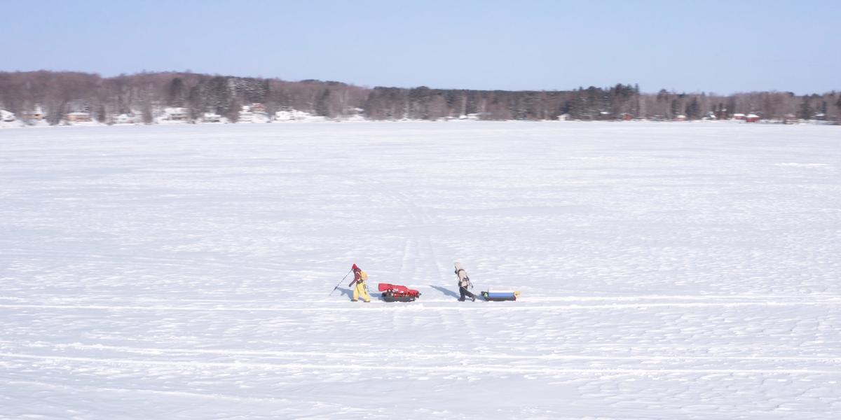 An aerial image of two UMD students pulling sleds across a frozen lake.