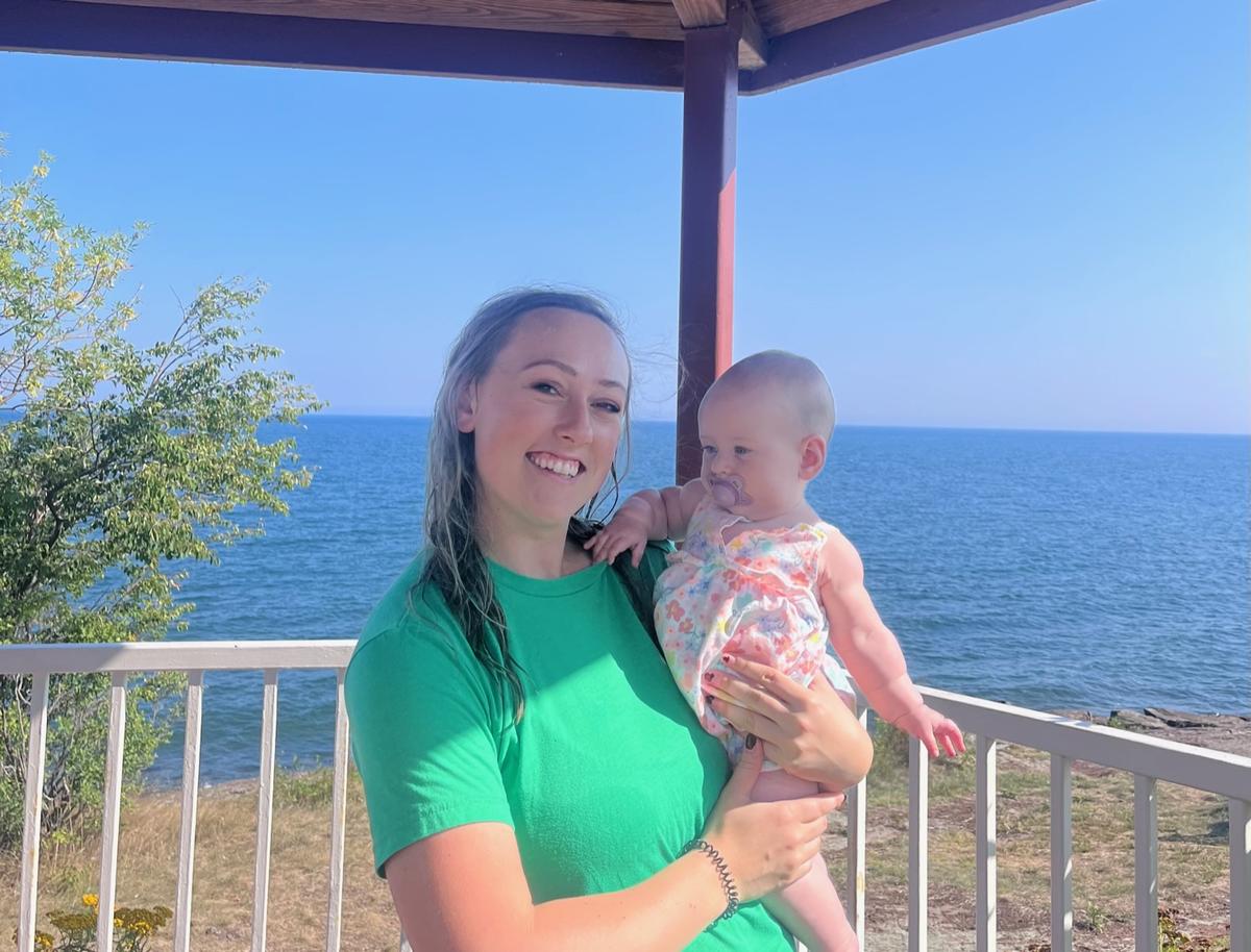 Liz Urbaniak holding her 1 year old daughter while standing near a lake
