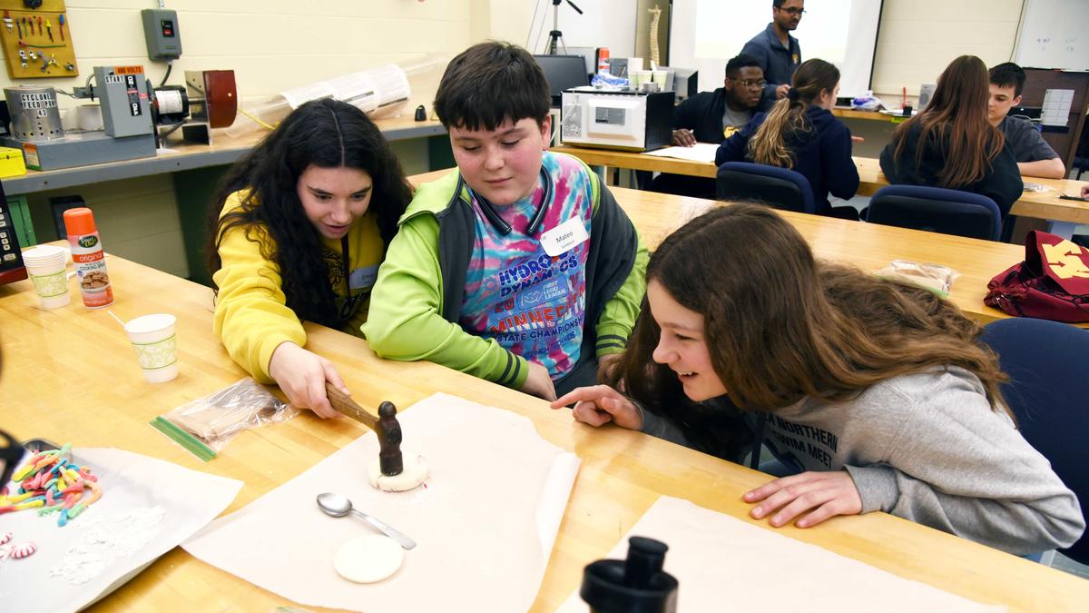Female UMD student working with two school kids on an experiment