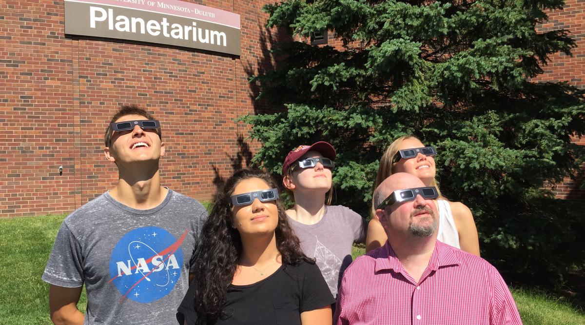 A group of UMD students and faculty view the sun with solar eclipse glasses.