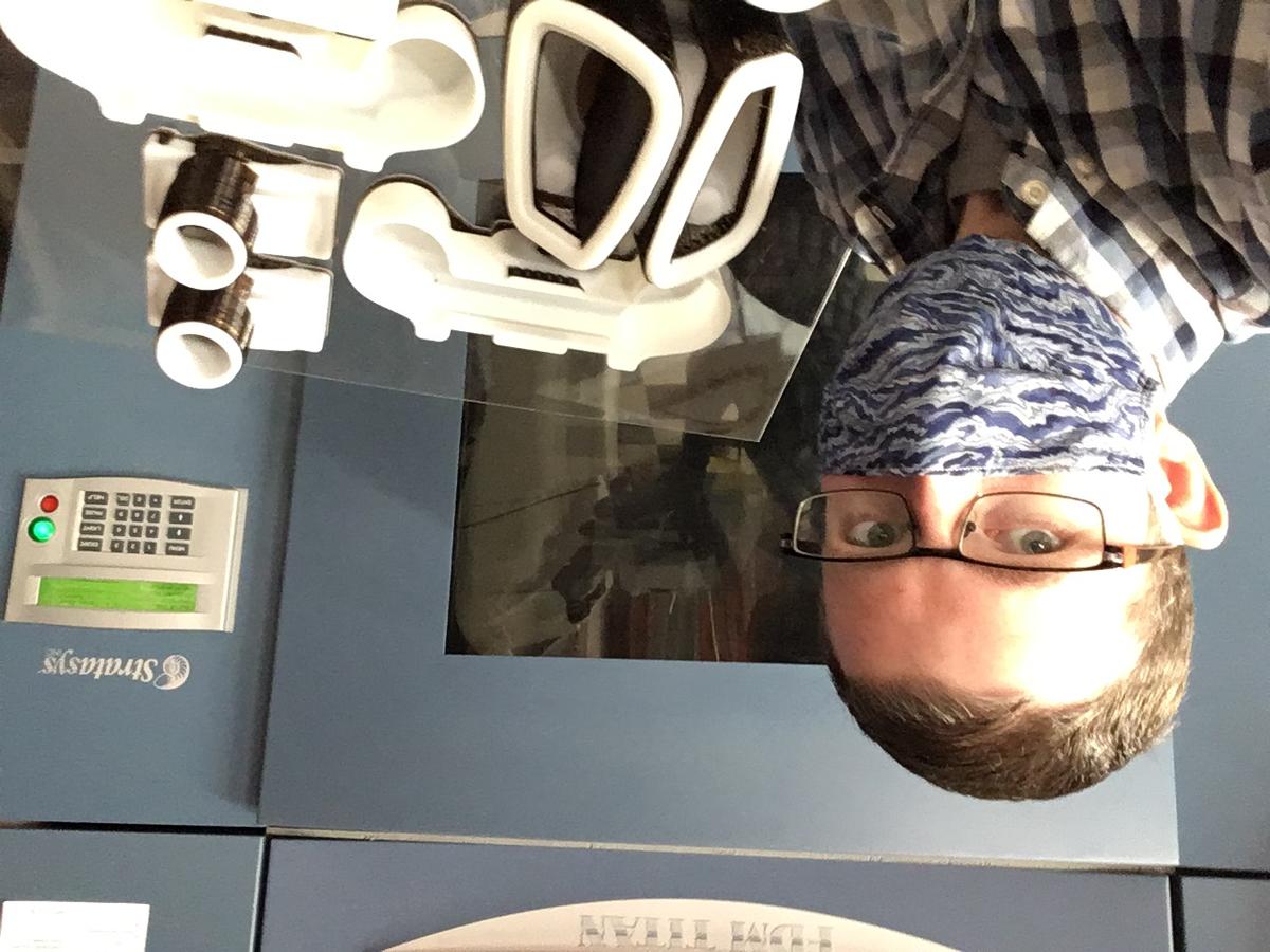 Kory Jenkins takes a selfie wearing mask as he stands in front of parts for PAPR respirators.