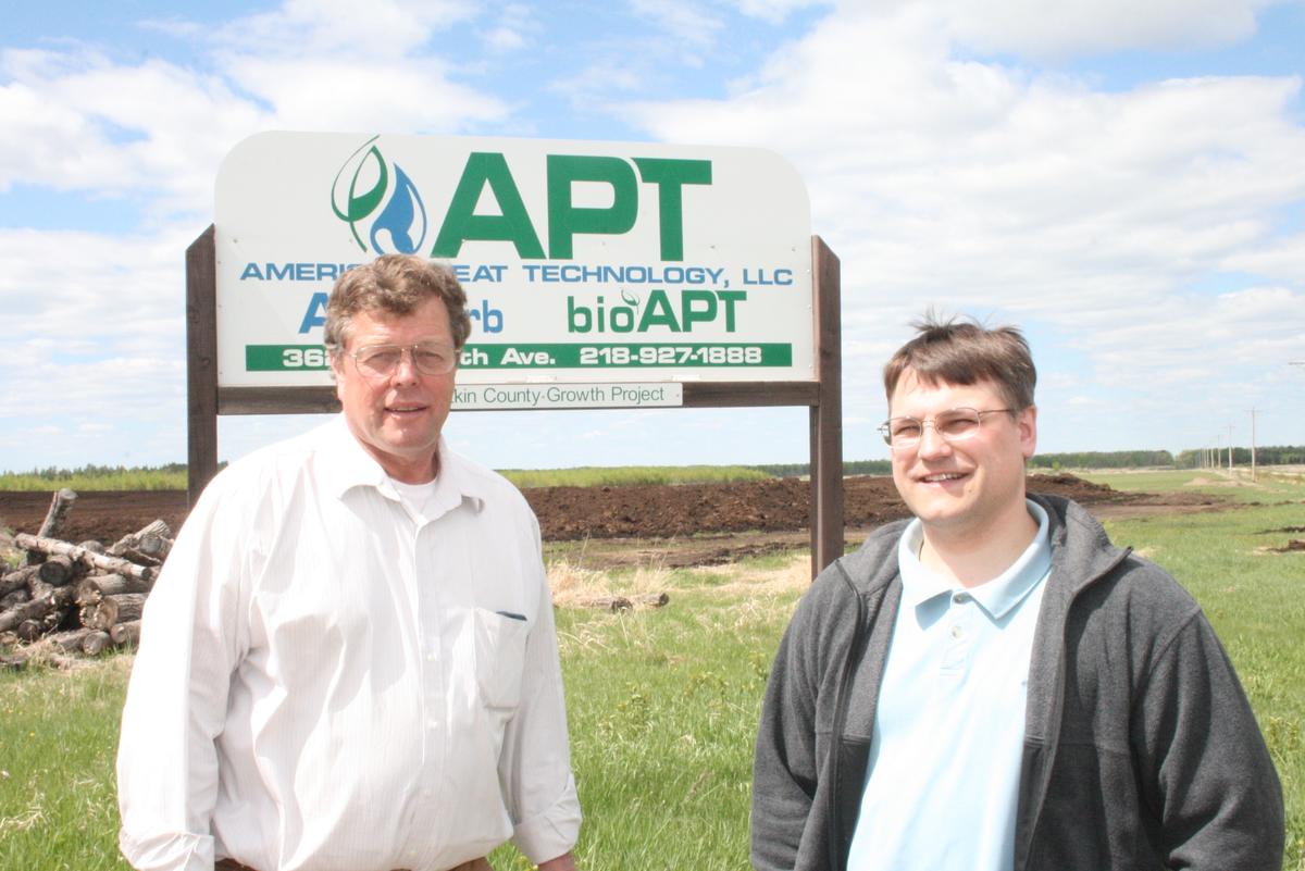 Two researchers in front of American Peat Technology, LLC sign at Aitkin County Growth Project site.