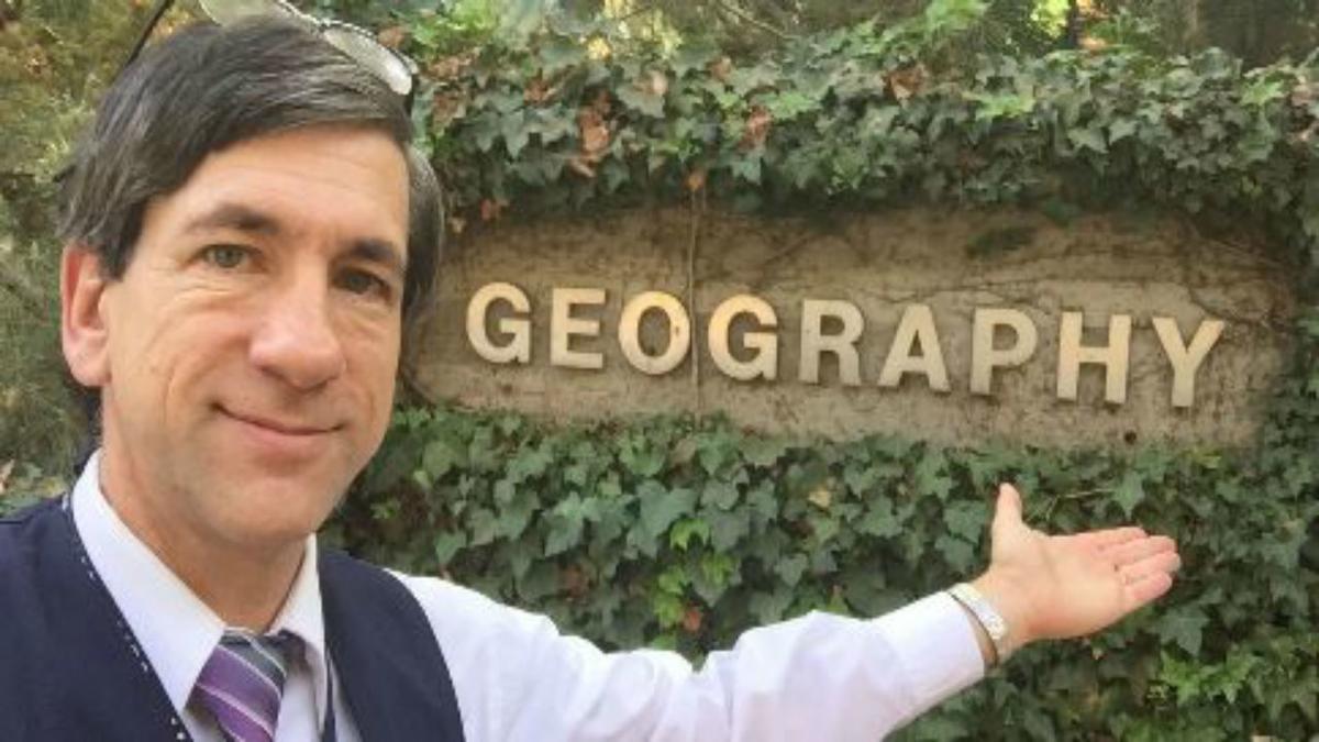 UMD Professor David Syring in front of a sign that says "Geography"
