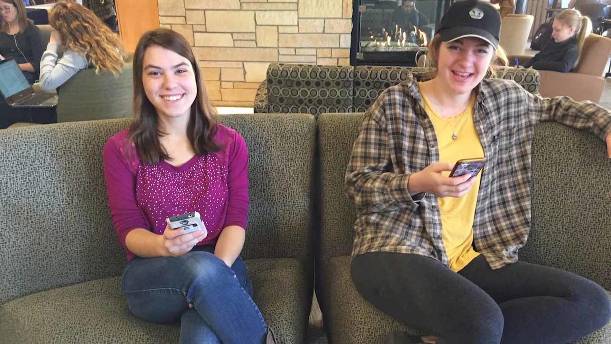 Corrin and Amanda sitting on a couch in Kirby Student Center on their cell phones