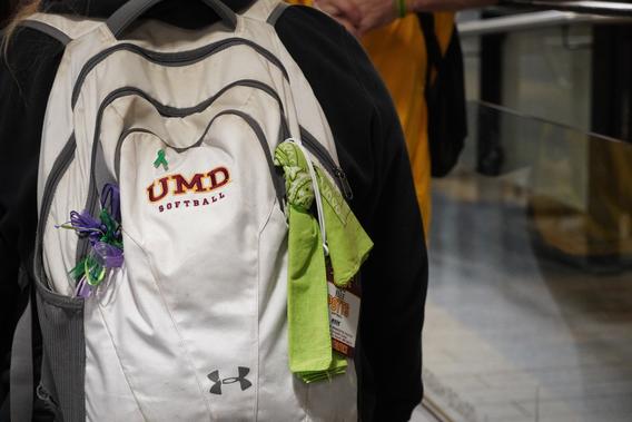 A white backpack branded with "UMD Softball" with a green bandana tied to it