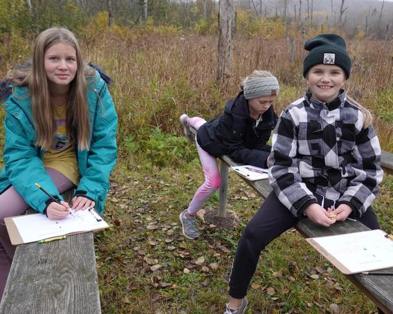 Three students from Lakewood Elementary work on their field journals in the school forest