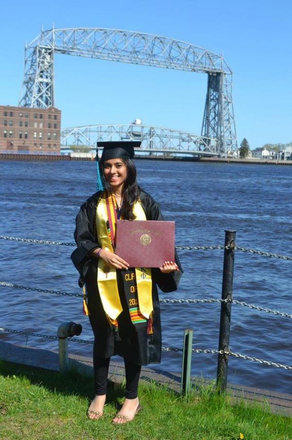 A proud UMD grad stands with her degree in front of the Duluth Aerial Lift Bridge.