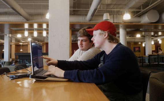 Two UMD students collaborate on programming homework around a laptop.