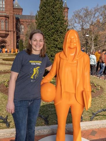 Lindsey Dietz standing next to an orange statue of herself holding a basketball and a laptop