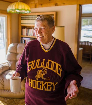 Bonnie Shea wearing a Bulldog Hockey jersey, holding a cup of coffee, and smiling while telling a story