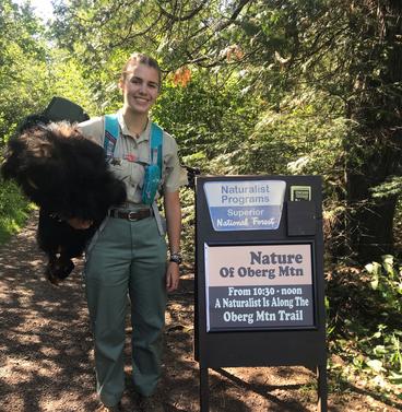 Elizabeth Ross holding a fur in front of a sign that reads " Naturalist programs lake superior national forest"