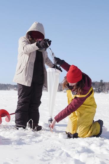 Two UMD students pull a zooplankton net from a hole in the ice on a frozen lake.