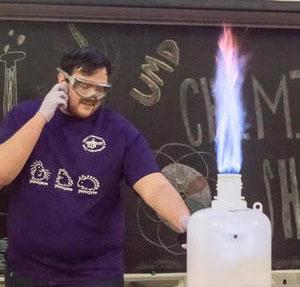Student doing a chemistry experiment with flames shooting out of a bottle. 