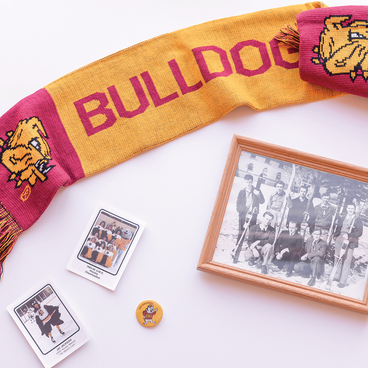 An image showing artifacts from UMD's history. A scarf, UMD mascot trading cards, pins, and ski team members photo.