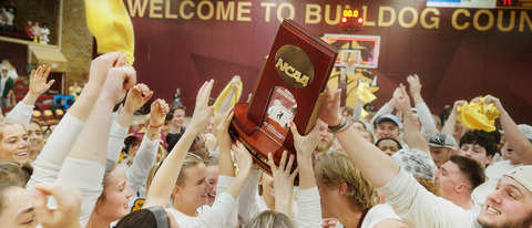Hands reach for a NCAA trophy in front of the Welcome to Bulldog Country Sign