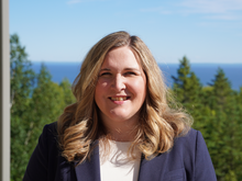 A headshot of Katie Gettman with Lake Superior and forest in the background