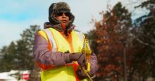 Manik Barman, Ph.D, conducts pothole and road infrastructure field research near UMD while wearing a furry hat, reflective vest and measuring tape.