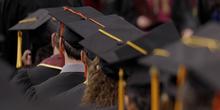 A row of students sitting at commencement wearing mortarboards, shown from the back