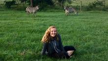 Katie Desautels sitting on grass with two zebras in the background